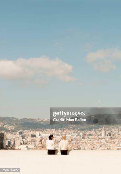 rear view of female tourists looking out over cityscape, barcelona, spain - skyscraper roof stock pictures, royalty-free photos & images