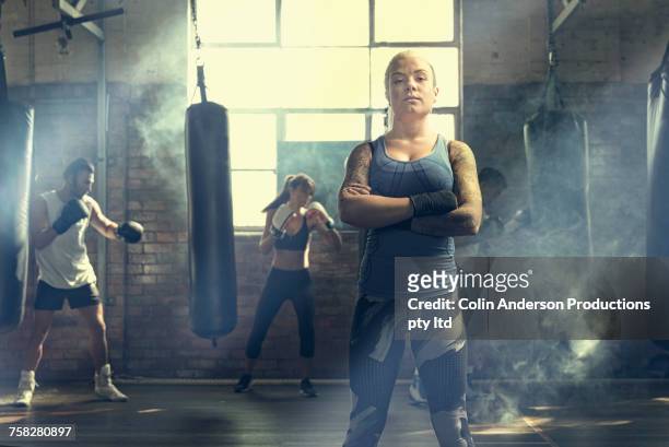 confident woman posing near punching bags in gymnasium - boxen sport stock-fotos und bilder