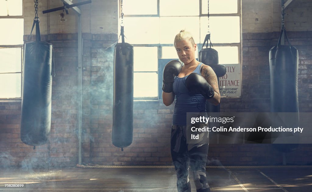 Confident Caucasian woman posing near punching bags in gymnasium