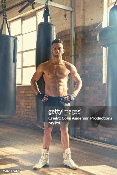 confident hispanic man posing near punching bags in gymnasium - fighter portraits stock pictures, royalty-free photos & images