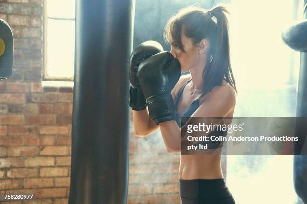 pacific islander woman hitting punching bag in gymnasium - female boxer stock-fotos und bilder