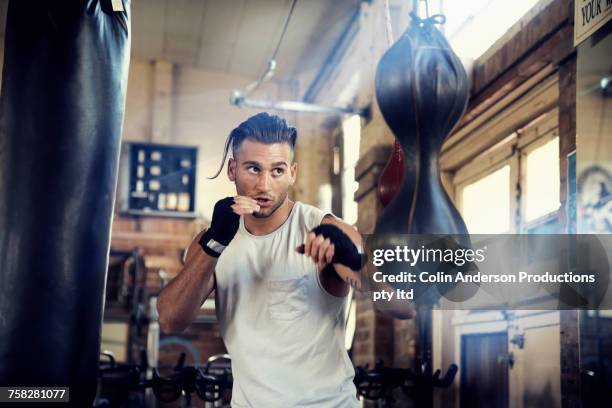 hispanic man punching speed bag in gymnasium - boxer stock-fotos und bilder