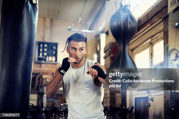 hispanic man punching speed bag in gymnasium - boxing young men stock pictures, royalty-free photos & images