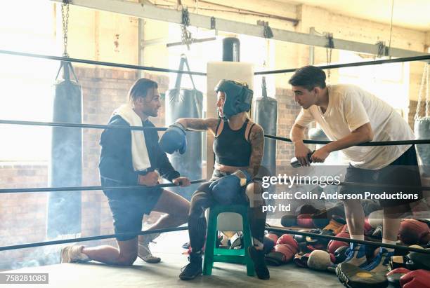 Trainers talking to boxer on stool in boxing ring