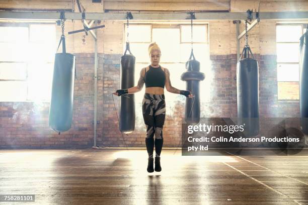 caucasian woman jumping rope in gymnasium near punching bags - warm up exercise stock-fotos und bilder