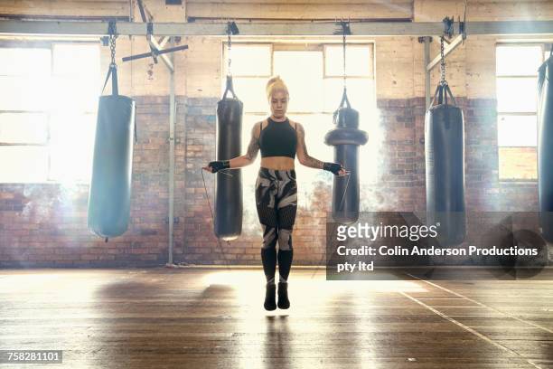 caucasian woman jumping rope in gymnasium near punching bags - skipping along stock pictures, royalty-free photos & images