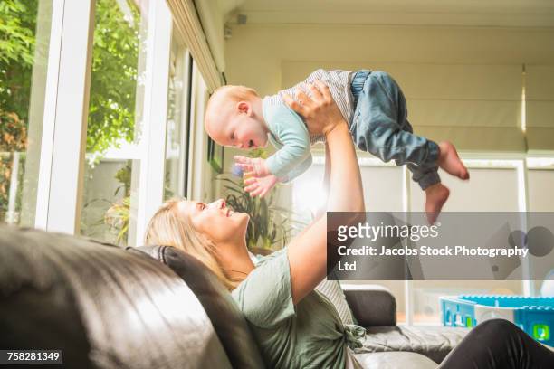 caucasian mother sitting on sofa lifting baby son - melbourne homes stock pictures, royalty-free photos & images