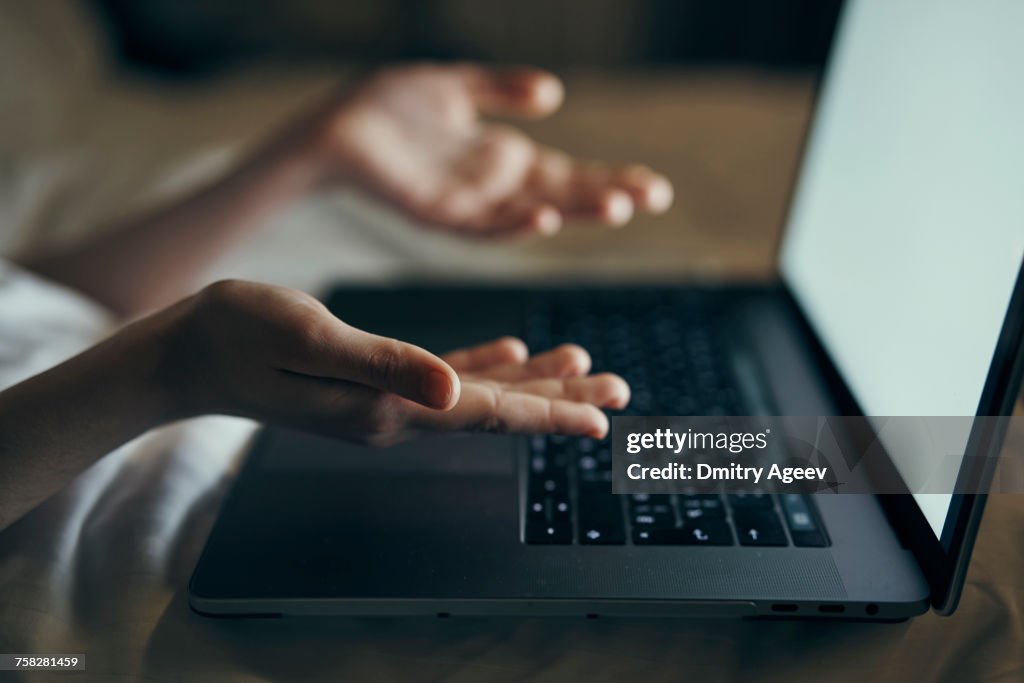 Hands of Caucasian woman gesturing at laptop in bed