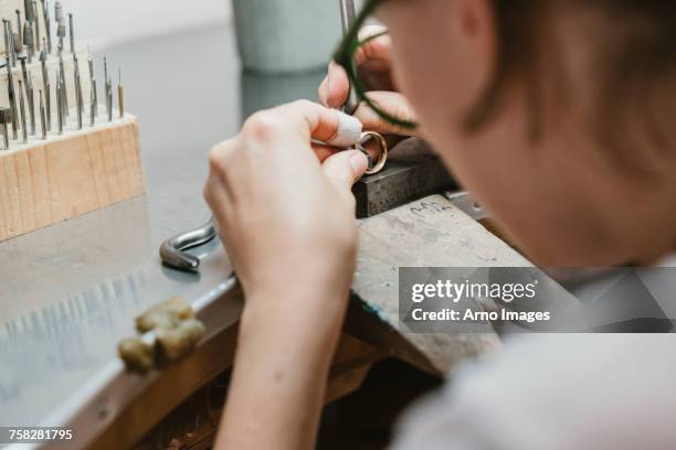 over shoulder view of female jeweller making ring at workbench - jewellery workshop ストックフォトと画像