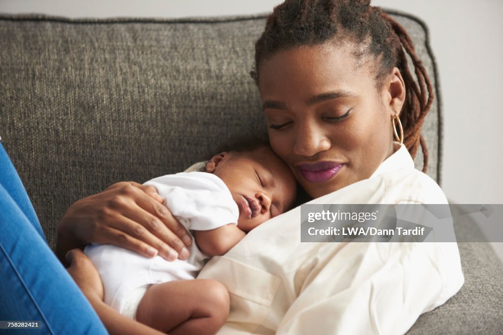 Black mother cuddling sleeping baby son on sofa