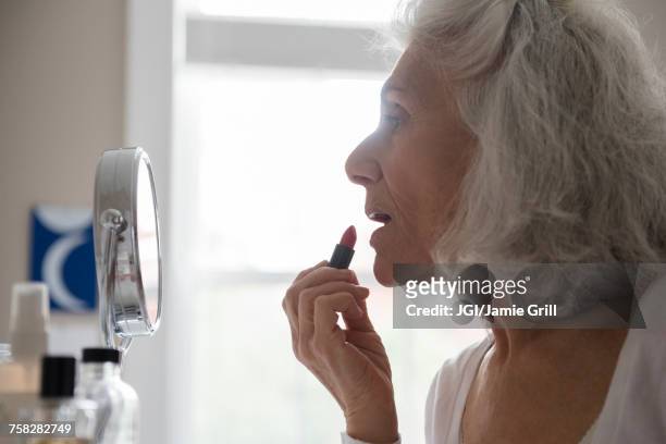 older woman applying lipstick in mirror - woman gray hair mirror stock pictures, royalty-free photos & images