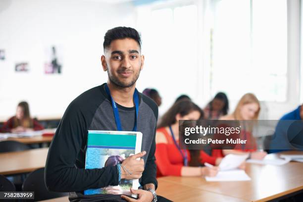 portrait of student in classroom holding textbook looking at camera smiling - indian boy portrait stockfoto's en -beelden