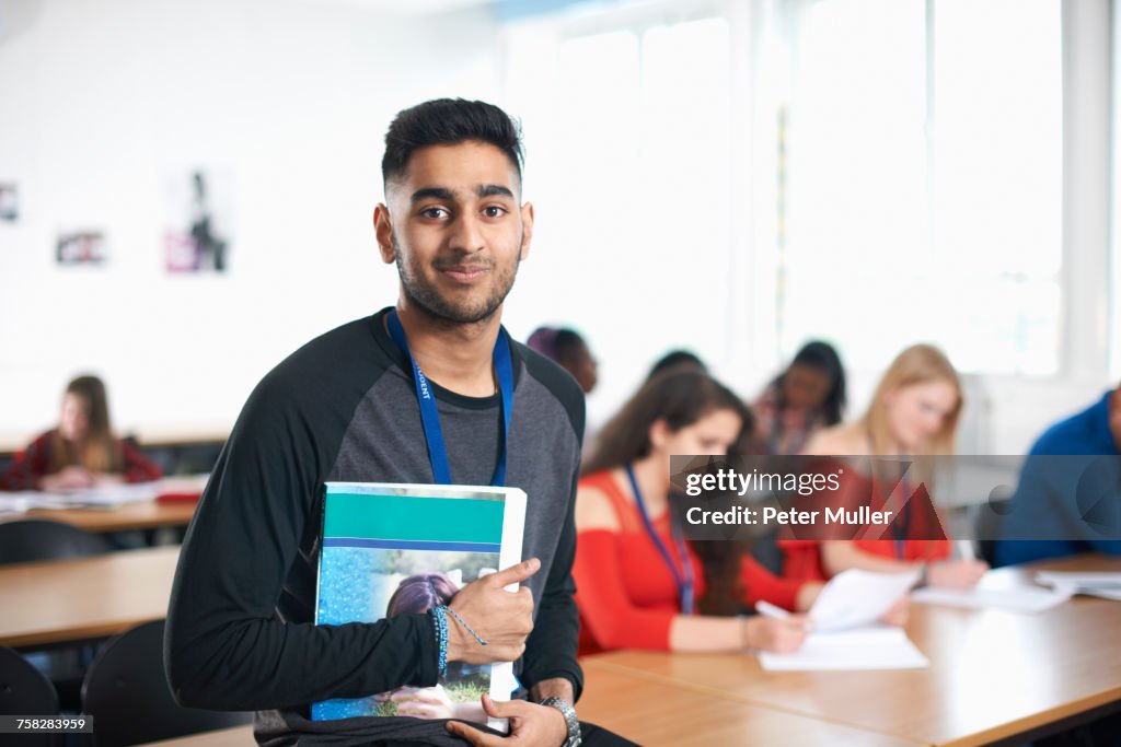 Portrait of student in classroom holding textbook looking at camera smiling