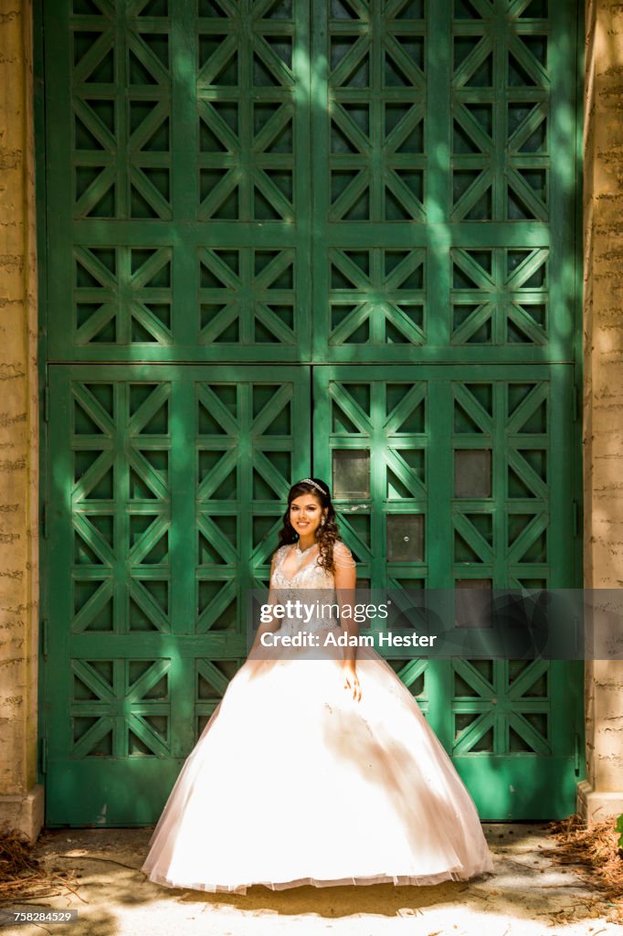 Smiling Hispanic girl wearing gown near green wall