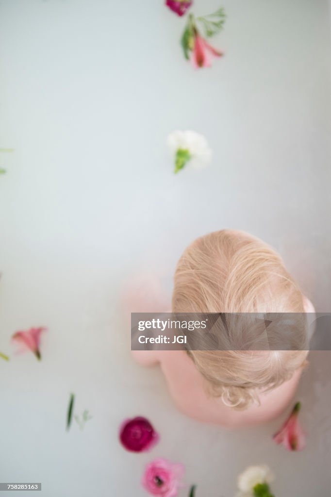 Caucasian baby boy in milk bath with flowers