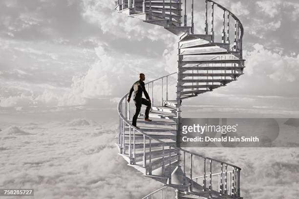 man climbing spiral staircase in the clouds - spiral staircase fotografías e imágenes de stock
