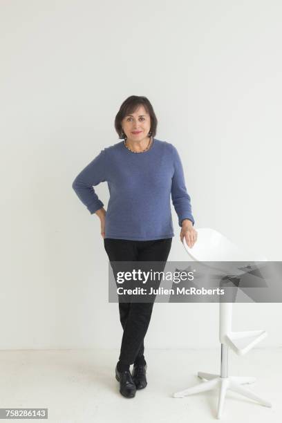 confident older mixed race woman leaning on stool - standing on chair stockfoto's en -beelden