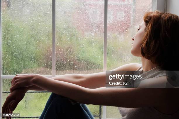caucasian woman sitting near rainy window daydreaming - window rain stock pictures, royalty-free photos & images