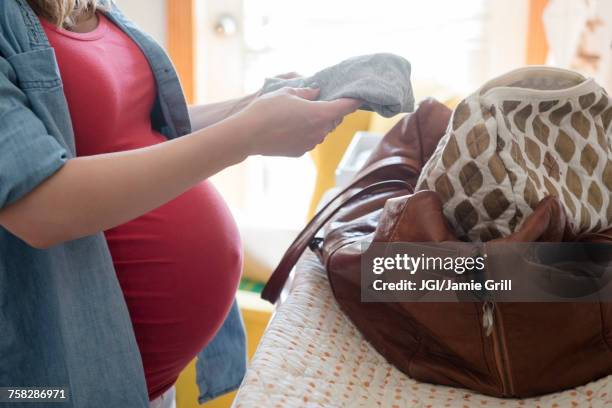 caucasian expectant mother putting clothing in the bag - diaper bag stock pictures, royalty-free photos & images