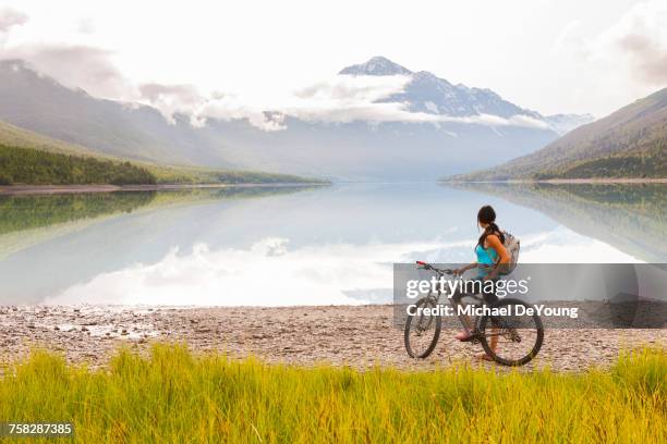 mixed race woman riding a bicycle near lake - anchorage foto e immagini stock