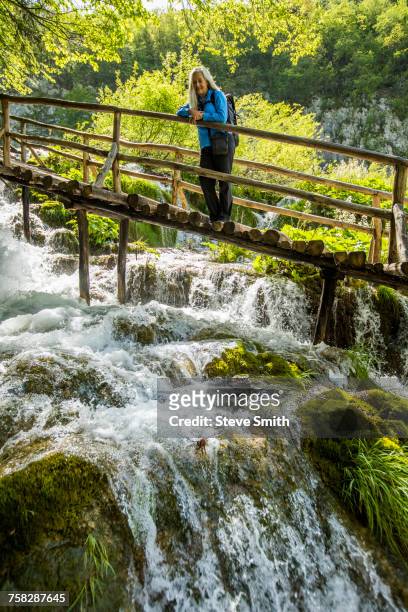 older caucasian woman on wooden footbridge admiring waterfall - plitvice stock-fotos und bilder