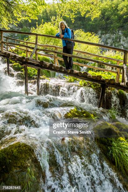 older caucasian woman on wooden footbridge admiring waterfall - plitvice lakes national park stock pictures, royalty-free photos & images