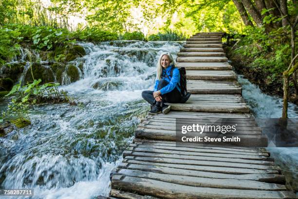 older caucasian woman sitting on wooden staircase over waterfalls - plitvice lakes national park stock pictures, royalty-free photos & images