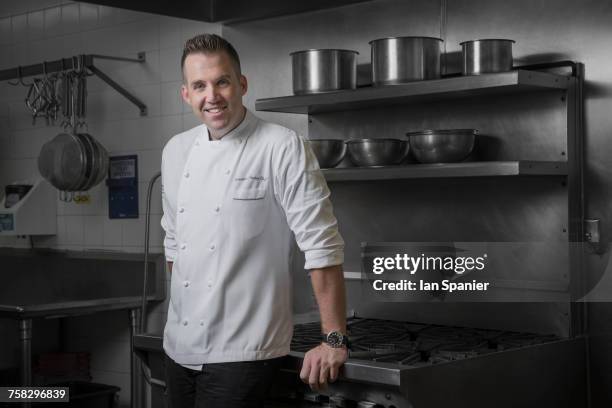 portrait of happy pastry chef leaning against hob in kitchen - beverly hills restaurant stock pictures, royalty-free photos & images