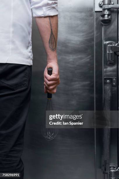 cropped rear view shot of pastry chef with whisk tattoo holding whisk in kitchen - pasteleiro imagens e fotografias de stock