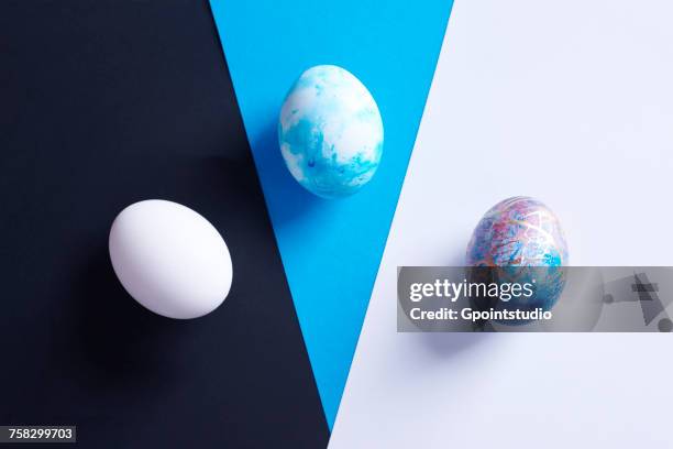 overhead view of three dyed easter eggs on blue, black and white shapes - easter poland stock pictures, royalty-free photos & images