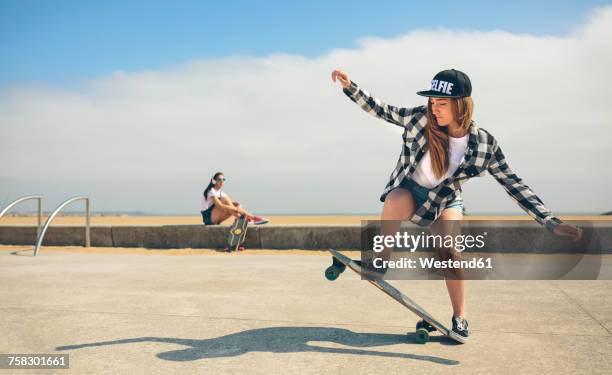 young woman longboarding while her friend watching her - estilo de vida alternativo fotografías e imágenes de stock