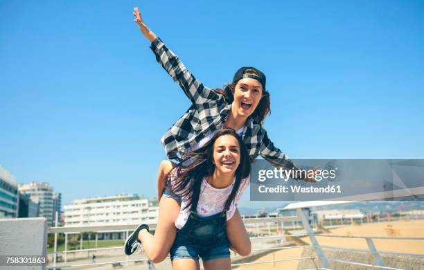 young woman giving her friend a piggyback ride on roof terrace - cavalitas imagens e fotografias de stock