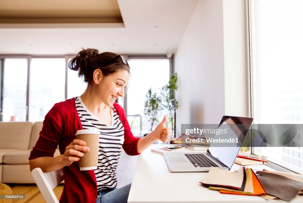 Smiling woman with coffee to go at desk at home