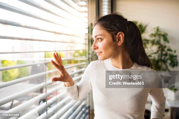 woman at home looking out of the window - jalousie stock-fotos und bilder