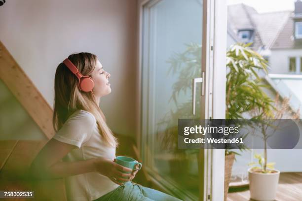 young woman relaxing at home with a cup of tea, listening music - listening stock-fotos und bilder