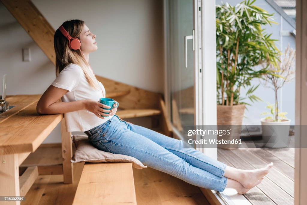 Young woman relaxing at home with a cup of tea, listening music