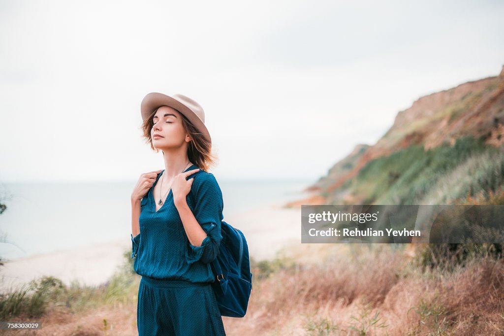 Mid adult woman in coastal setting, carrying backpack, breathing in fresh air