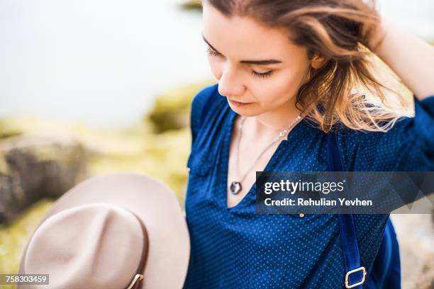 mid adult woman in coastal setting, holding hat, touching hair - ruffling stock pictures, royalty-free photos & images