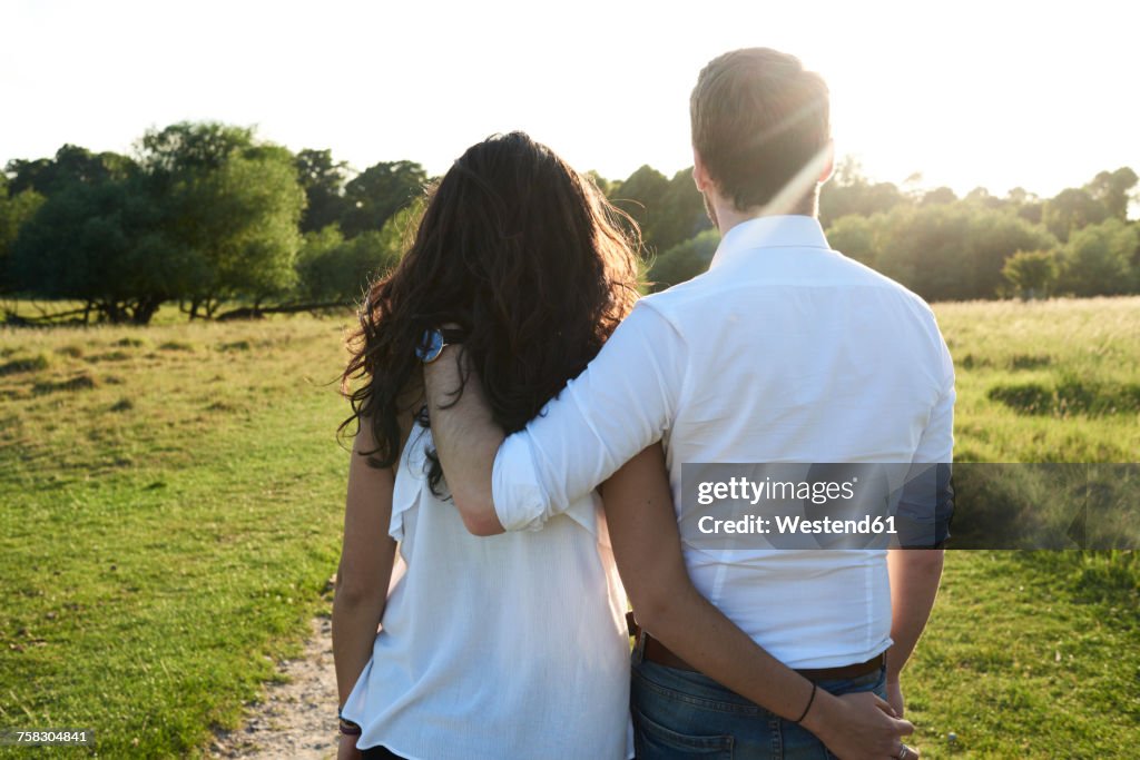 Back view of young couple arm in arm at sunset