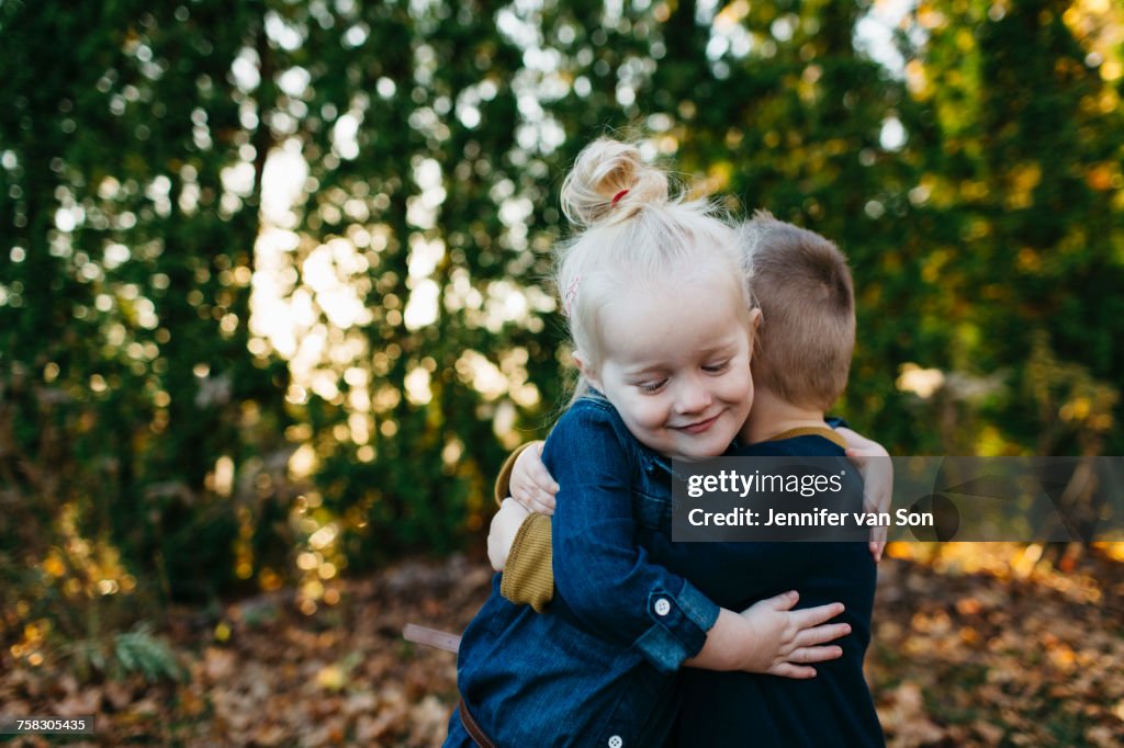 Cute female toddler hugging twin brother in autumn garden