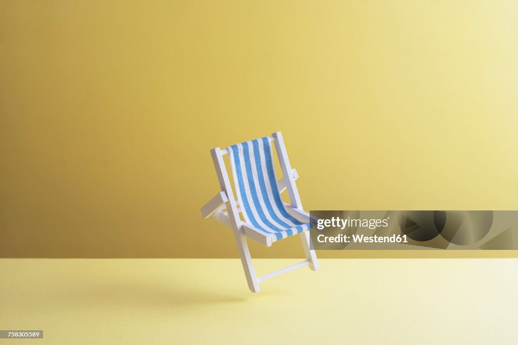 Single beach chair hovering in the air in front of yellow ground, 3D Rendering