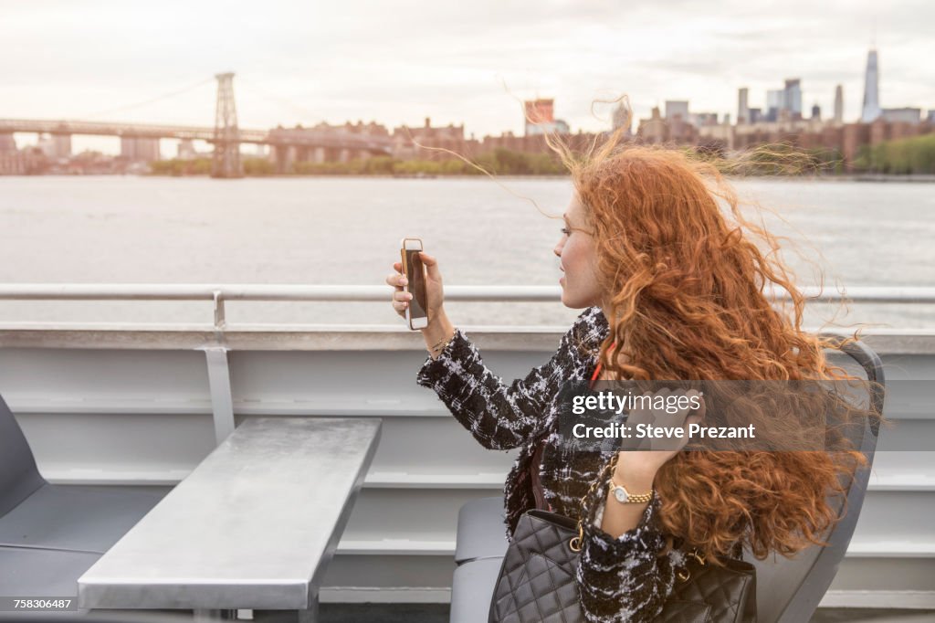 Young businesswoman on passenger ferry deck taking smartphone selfie