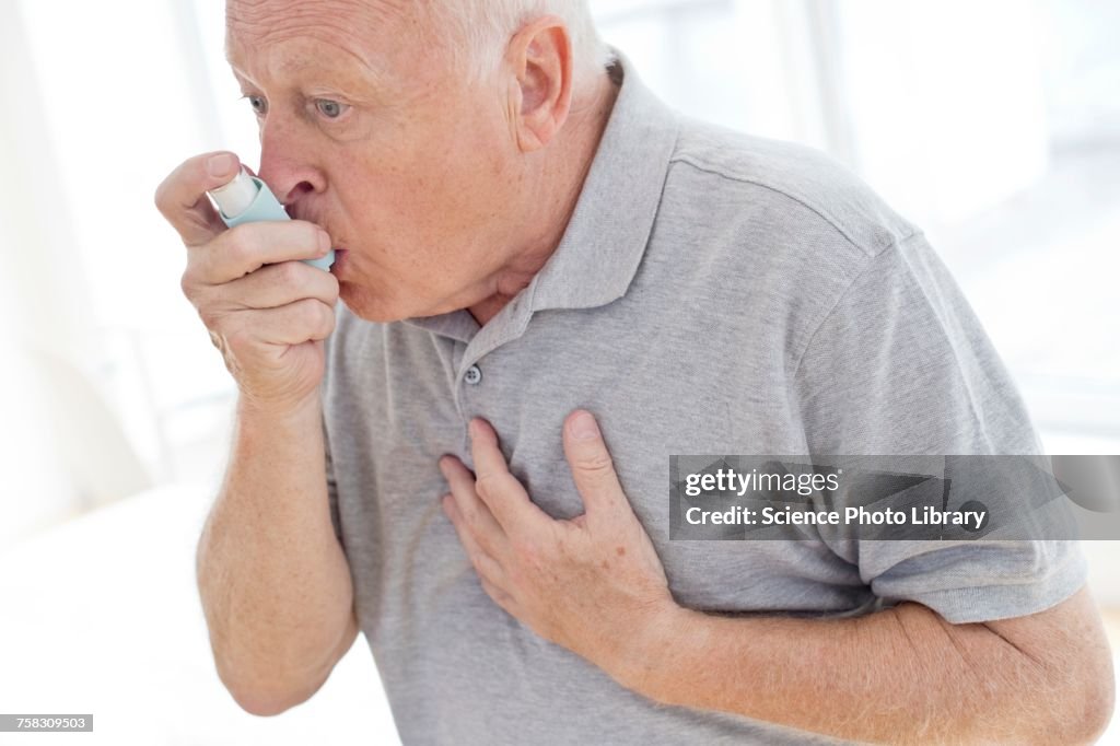 Senior man using inhaler, holding chest