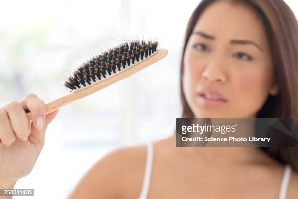 woman holding hairbrush with worried expression - haarausfall stock-fotos und bilder