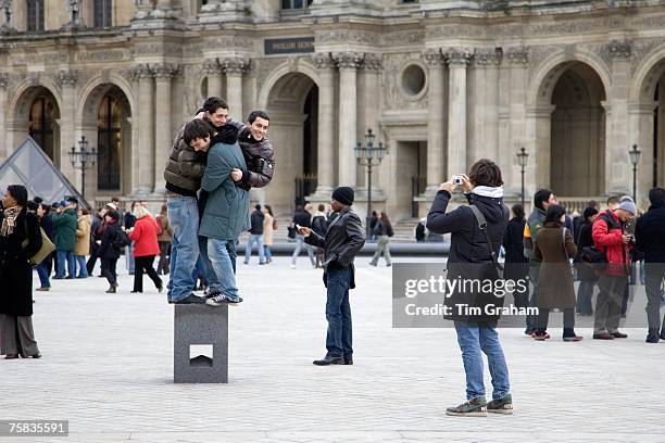 Young tourists having fun trying to balance on posing plinth outside the Louvre Museum, Central Paris, France