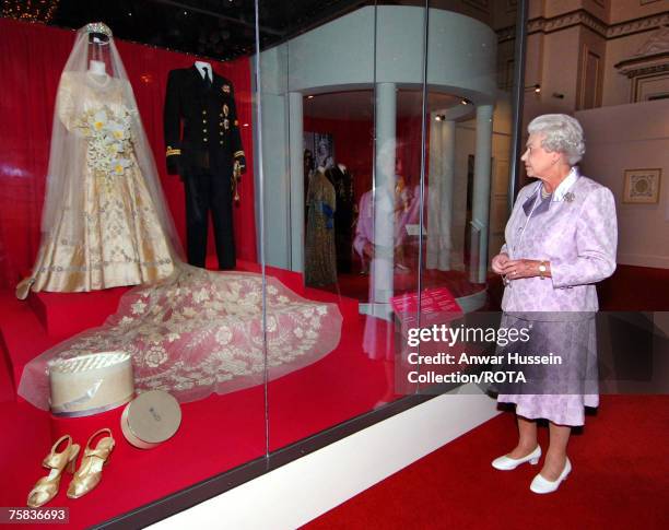 Queen Elizabeth looks at her 1947 wedding gown and 13 foot bridal trail designed by Norman Hartnell with the naval uniform worn by Prince Philip,...