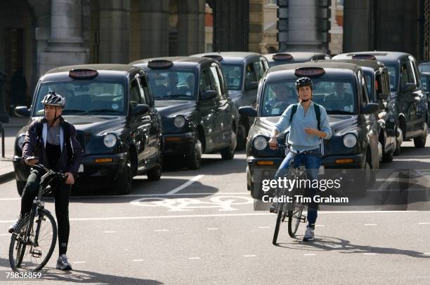 Two cyclists and black taxis in traffic waiting in Trafalgar Square, downtown London city centre, England, United Kingdom