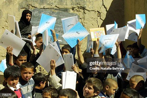 Afghan boys at Kabul's Amir Dost Mohammad Khan Secondary School hold up their newly distributed textbooks in a destroyed classroom March 25, 2002 in...