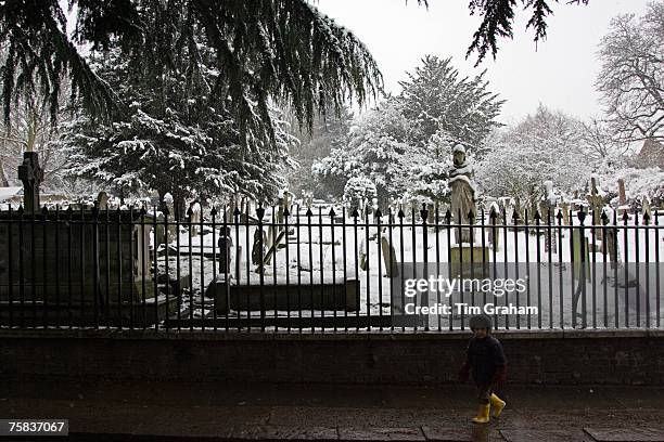 Young boy walks past snow covered graveyard, London, United Kingdom