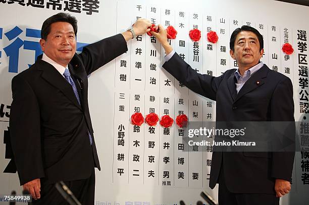 Japanese Prime Minister Shinzo Abe and Hidenao Nakagawa of the Liberal Democratic Party place roses above names of elected candidates, at the head...